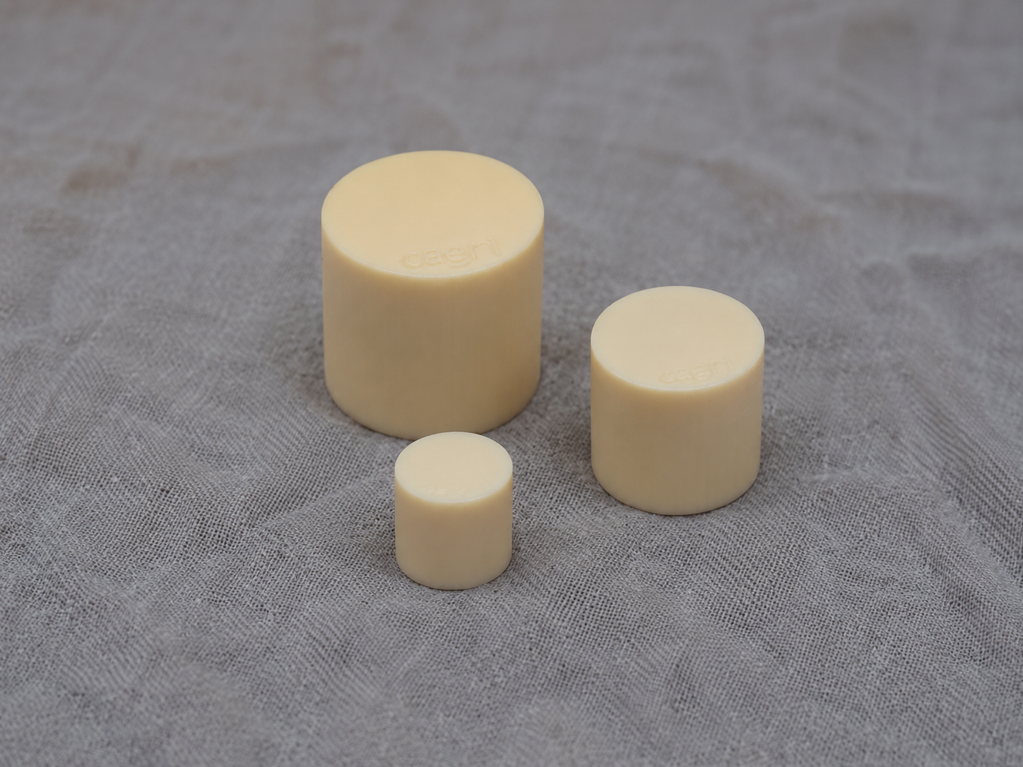 Three cylindrical dose-calibrator sources against grey fabric.